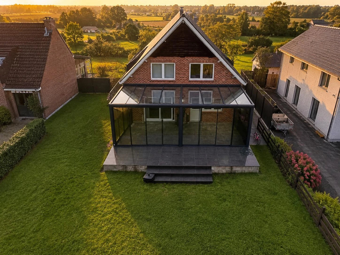 Woning met een glazen aanbouw over de volle achtergevel, van bovenaf gezien bij zonsondergang, geplaatst door SAVA Glass