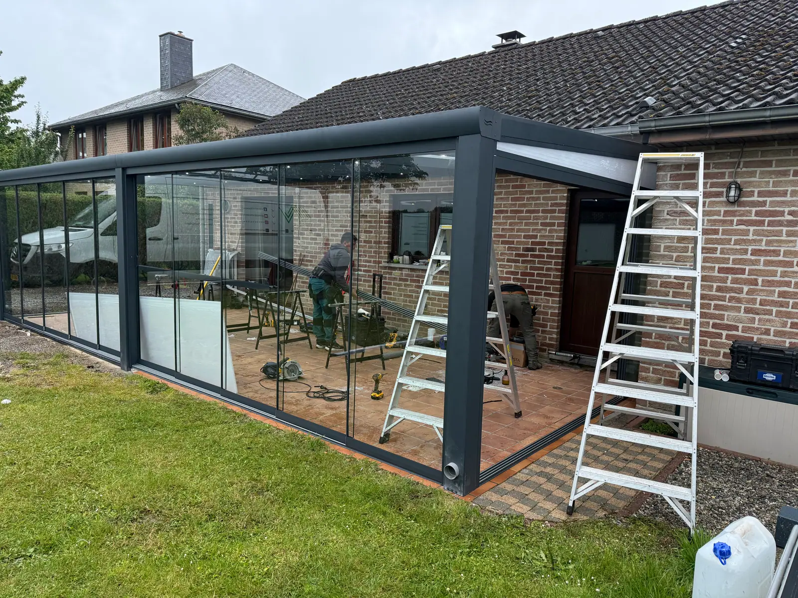 Twee monteurs van SAVA Glass bouwen een veranda op bij een klant thuis, met ladders en gereedschap
