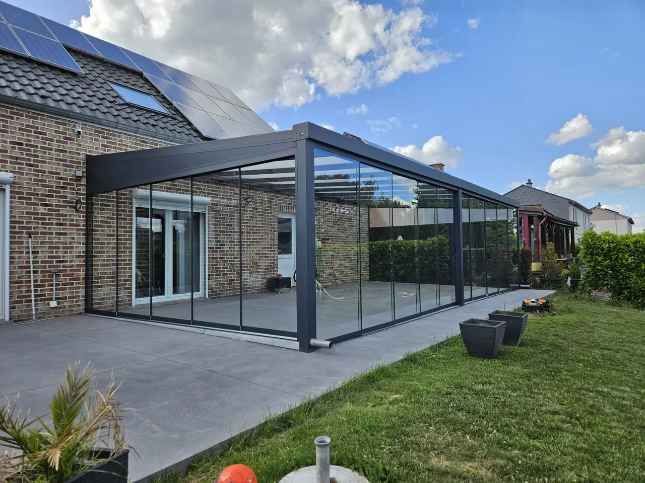 Antracietkleurige aluminium veranda met glazen dak en glazen schuifwanden rondom