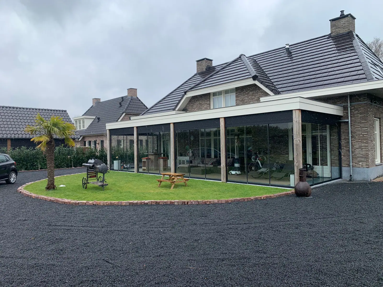 Brede veranda langs de gevel met houten staanders en glazen schuifwanden, om de hoek doorlopend